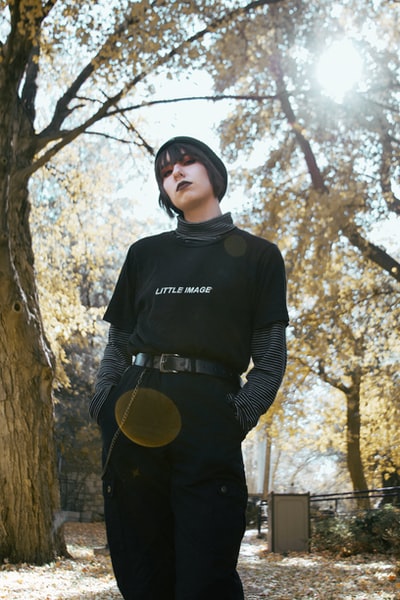 白天，一个穿着黑白长袖衬衫的男人站在棕色的树旁